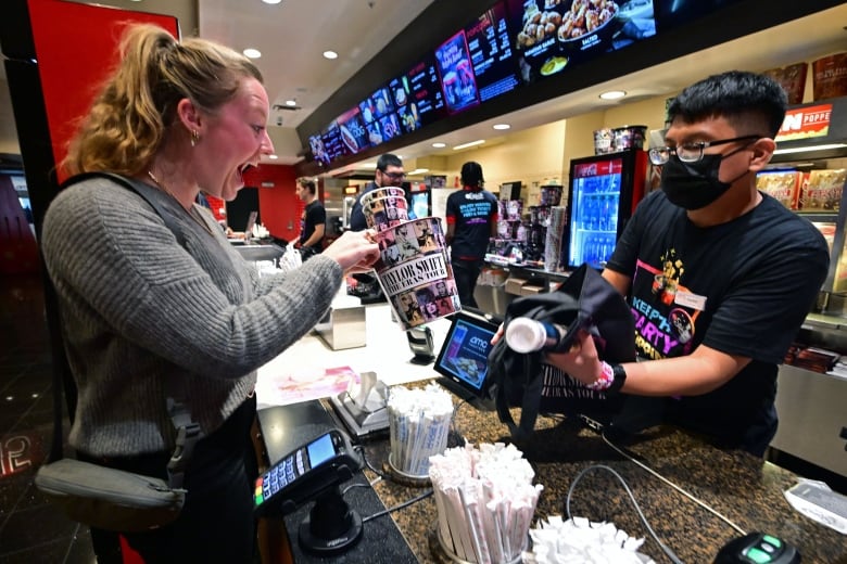 A person reacts while buying merchandise from a movie theatre cashier.
