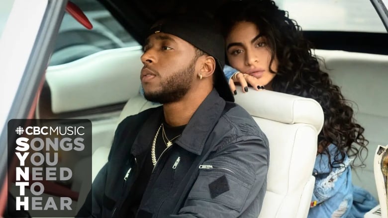 6lack is a Black man with a neatly trimmed beard sitting in the front seat of a car looking left. He's wearing a black jacket, black backwards cap, and has a small stud earing. Behind him is jessie Reyez, a woman with light brown skin and long black wavy hair, looking directly into the camera. She is leaning on the back of the driver's seat and has visible blue nail polish and is wearing a light blue outfit that may be denim. 