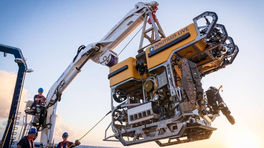 An ROV being hoisted above the water by a small crane.