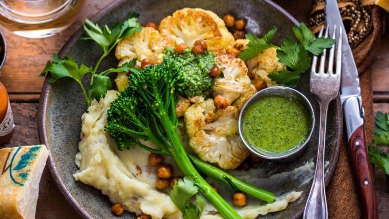 Overhead shot of a dinner plate on a wooden table. The plate has roasted cauliflower, creamy goat cheese mash, roasted chickpeas and broccolini.