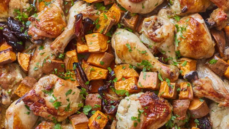 Closeup, overhead shot of roasted sweet potato chunks, dates, chicken thighs and drumsticks on a sheet pan. 