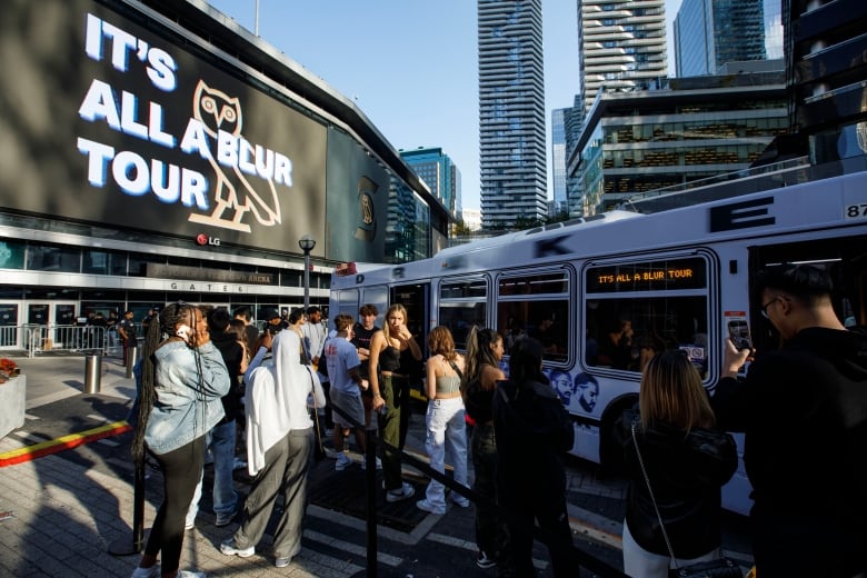 Fans of Drake standing outside Scotiabank Arena ahead of a concert, with a merchandise bus parked out front.