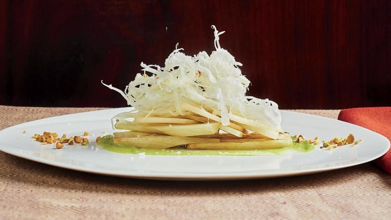 Side view of a white plate with a salad of sliced pear and fennel on it, topped with pecorino cheese. 