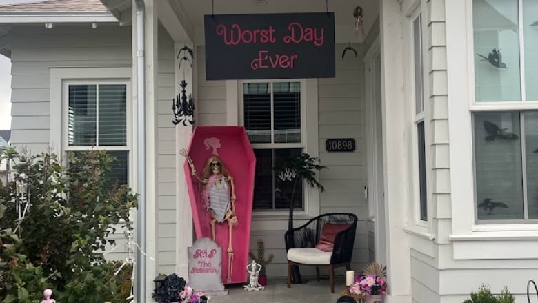 Skeleton in pink coffin with dead flowers in pink pots and a sign that says worst day over above the porch 