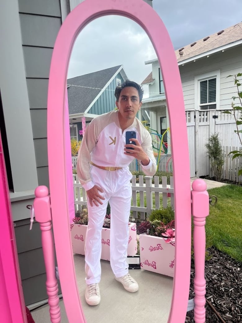 A man in a disco suit snaps a selfie in a bright pink mirror on a front porch.