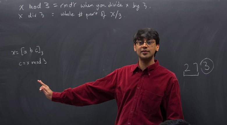 Canadian mathematician Manjul Bhargava in front of a chalkboard with math equations facing the class.