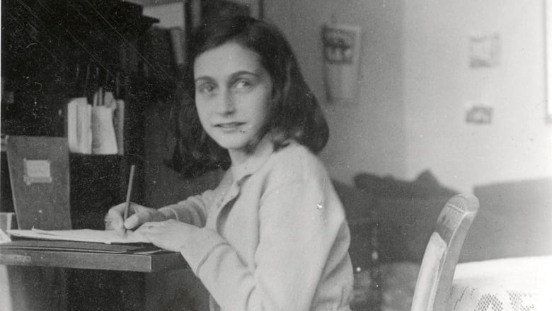 A faded black and white image of a petite teenage girl sitting at a desk and writing. She has shoulder-length dark hair and is turning to one side to look at the camera.