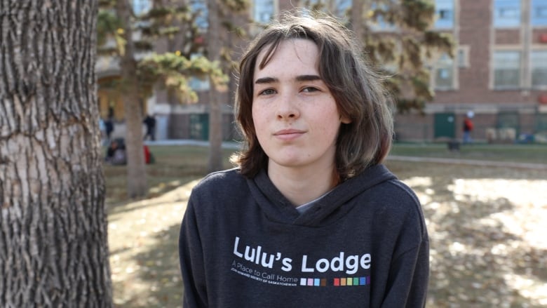 A youth poses in front of a building. They are wearing a black hoodie with Lulu's Lodge emblazoned on it. 