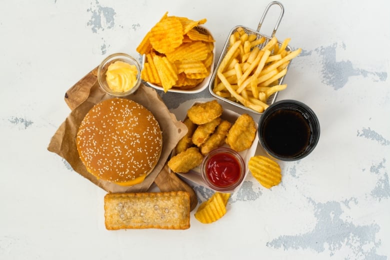 Viewed from above, a group of foods including a burger, fries, chips, chicken nuggets, and a glass of pop. 