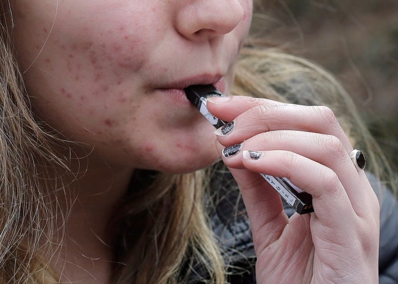 A young woman uses a vaping device.